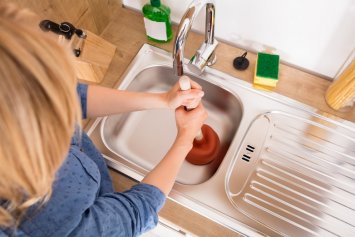 woman unclogging a sink in the kitchen