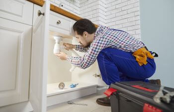 A plumber unclogging pipes under a kitchen sink.