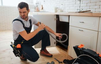 A plumber turning his head away due to aodor from kitchen sink drain.